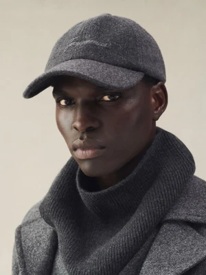 Model Badhiel Lony Nyang wearing a grey wool cap and ribbed knit cowl neck against a neutral seamless studio backdrop.