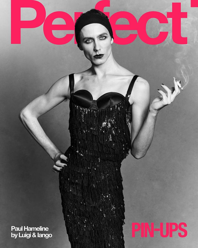 Person in a fringed dress holding a cigarette in a black-and-white magazine cover shoot against a grey backdrop and bold typography.