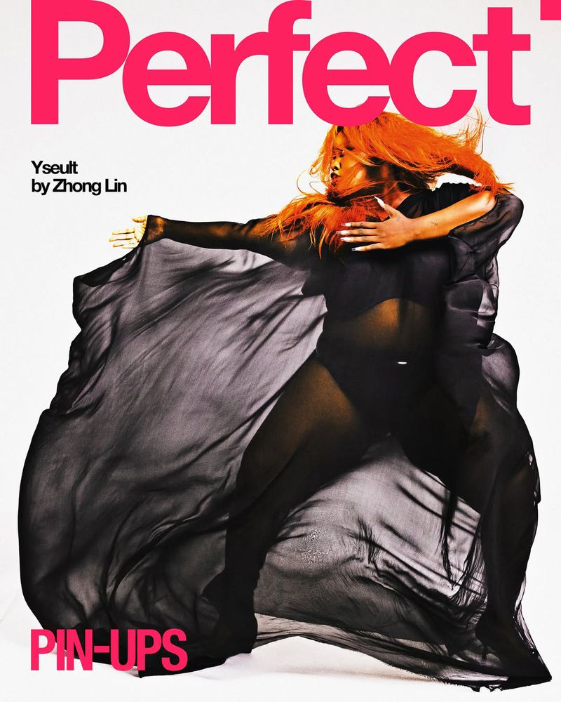 Magazine cover featuring a woman in a black bodysuit and flowing fabric, with red hair against a white backdrop and pink text.