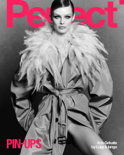 Black-and-white fashion photo of a model wearing a feathered collar and trench coat, posing in front of a pink magazine cover.