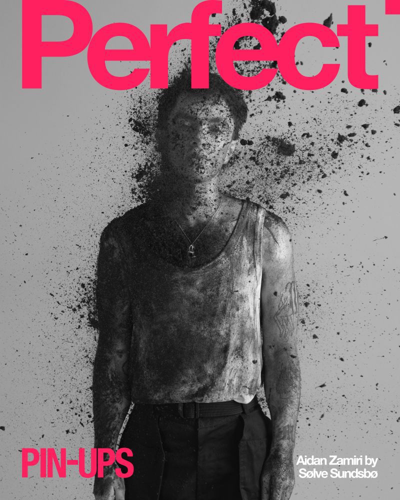 Magazine cover featuring a person with dark dust on their face and body, wearing a tank top and trousers against a gray background.