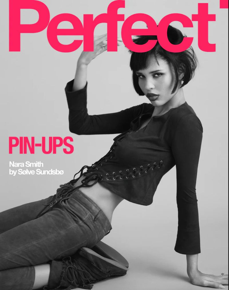 Fashion magazine cover featuring a model, Nara Smith, in a black lace-up top and grey jeans, posing against a grey background.