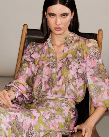 Model Alice Ferazzoli seated in a wooden chair wearing a pink and olive green floral printed long sleeve dress.