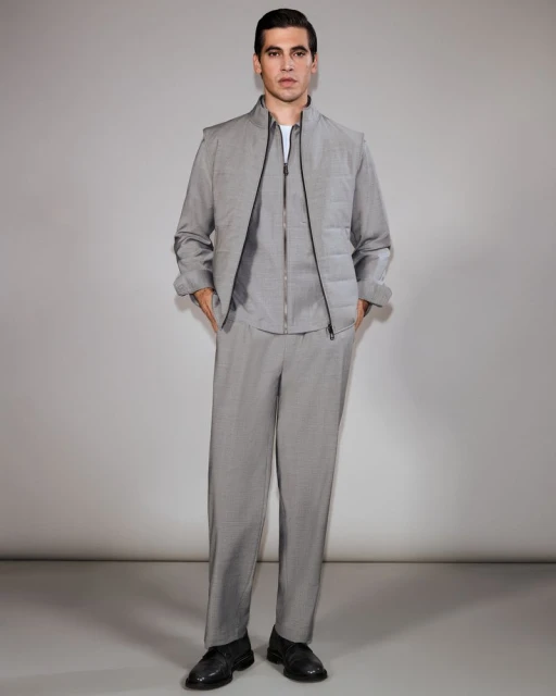 Full-length studio shot of a young adult male model wearing a gray casual suit. He poses with his hands in his pockets against a plain backdrop.