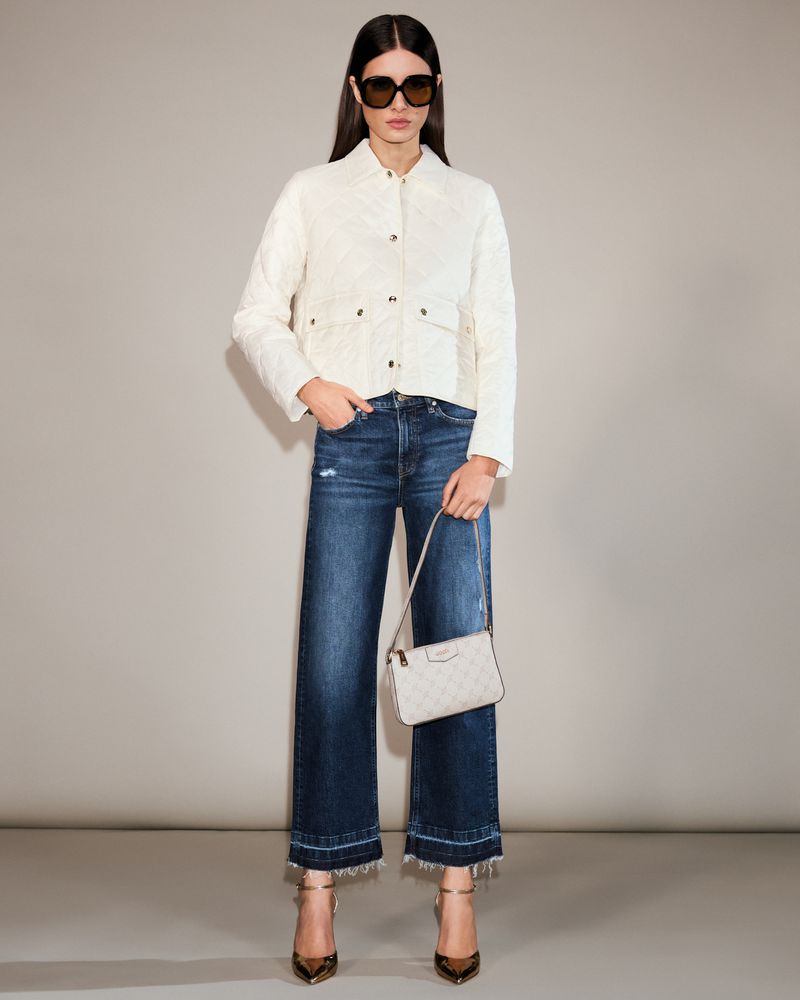 Model Alice Ferazzoli poses in a cream quilted jacket, dark wash wide-leg jeans, sunglasses, and heels against a grey studio backdrop.