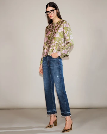 A woman models a floral top, blue jeans, and gold heels in a studio setting, full shot. Fashionable attire for women.
