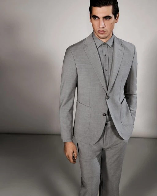 Man in gray suit and matching shirt poses in a photo studio with soft, diffused lighting. Fashion editorial portrait.
