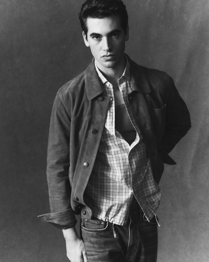 Model Marco Bellotti posing in a suede overshirt, open plaid shirt, and jeans in a black and white studio portrait for JOOP!.