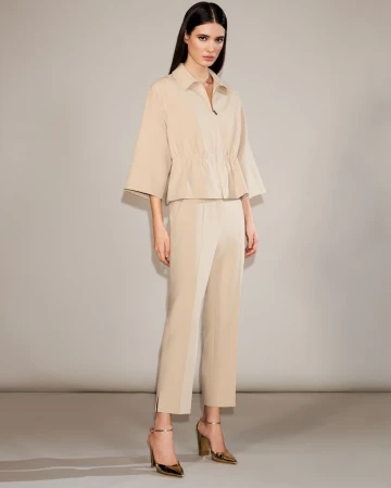 Alice Ferazzoli posing in a beige collared jacket and matching cropped trousers with metallic heels against a neutral studio backdrop.