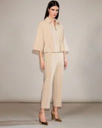 Alice Ferazzoli posing in a beige collared jacket and matching cropped trousers with metallic heels against a neutral studio backdrop.