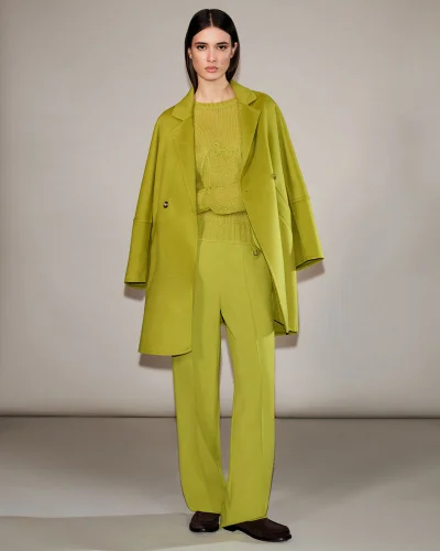 Model wearing a chartreuse wool coat, matching knit sweater, and trousers against a neutral grey studio backdrop.