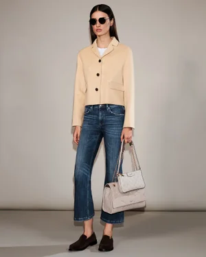 Model Alice Ferazzoli in a beige cropped jacket, blue jeans, sunglasses, and carrying two shoulder bags against a neutral backdrop.