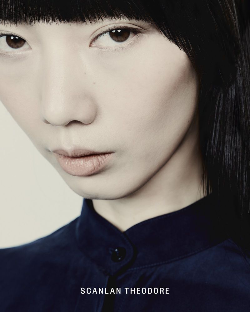 Portrait of a young Asian woman with dark hair wearing a navy top, captured in a close-up shot with soft, diffused lighting.