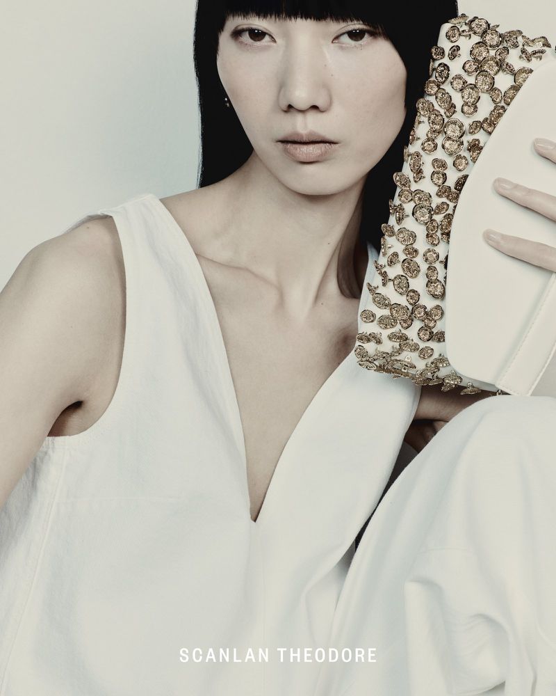 Model with dark hair holding an embellished white clutch against a neutral background for Scanlan Theodore.