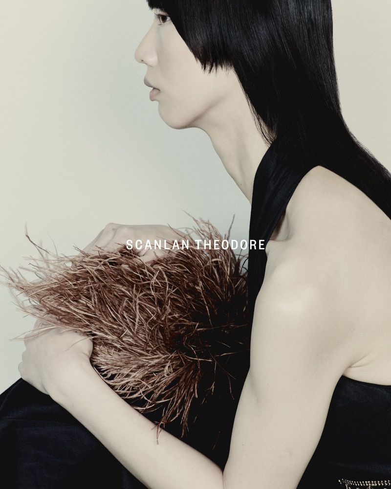 Profile shot of an Asian woman with blunt bob and black sleeveless top, holding a brown feathered object, in a studio setting.