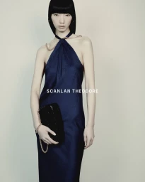 Model Yixin Zhao wearing a navy halter dress with chain strap details and holding a black clutch against a neutral background.