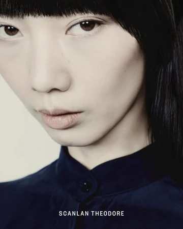Close-up portrait of model Yixin Zhao with straight black bangs wearing a dark navy buttoned shirt for Scanlan Theodore.