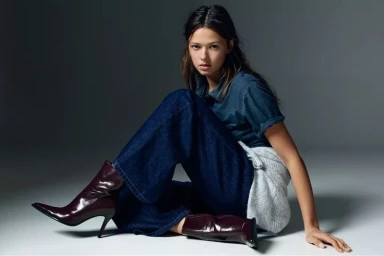 Model Didi Sviridova seated on a studio floor wearing dark denim jeans and burgundy pointed-toe stiletto boots for Pull&Bear.