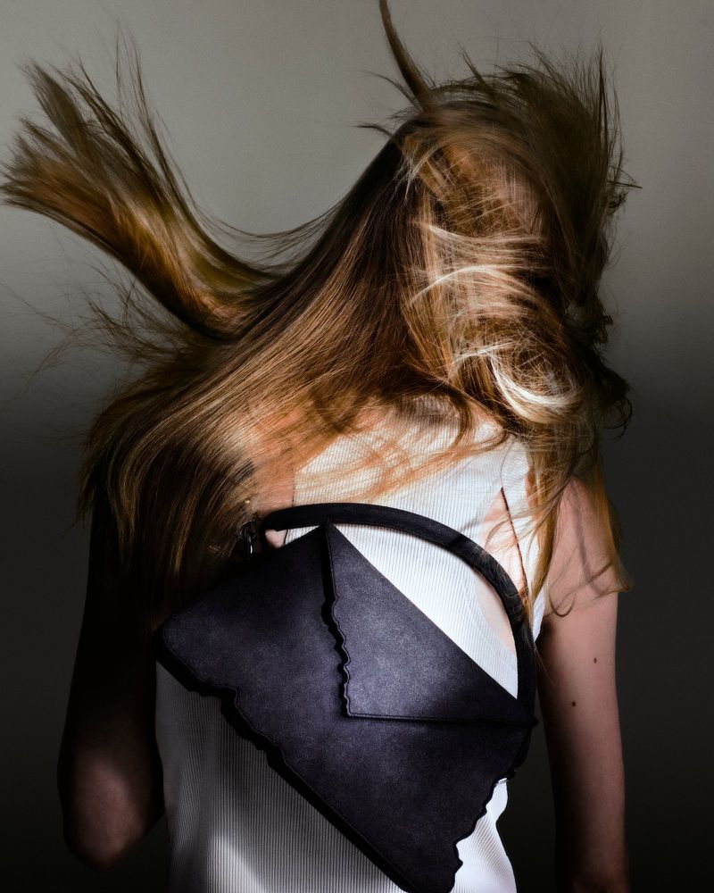 A fashion shot showcases a woman from the back with flowing blonde hair and a unique black and white handbag slung over her shoulder.