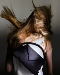 Model with long hair whipping across face wearing white top and black bag for Camper