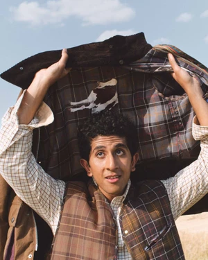 Man holding open a plaid-lined Barbour jacket above his head while wearing a check vest and collared shirt.