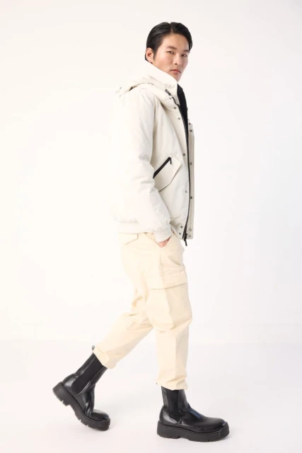 A stylish Asian man walking in a hooded jacket, cargo pants, and platform boots against a clean white background, fashion forward.