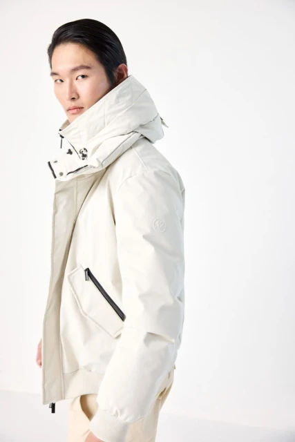 Asian man in winter fashion: wearing a hooded puffer jacket in a studio setting, showcasing the jacket's design and style.