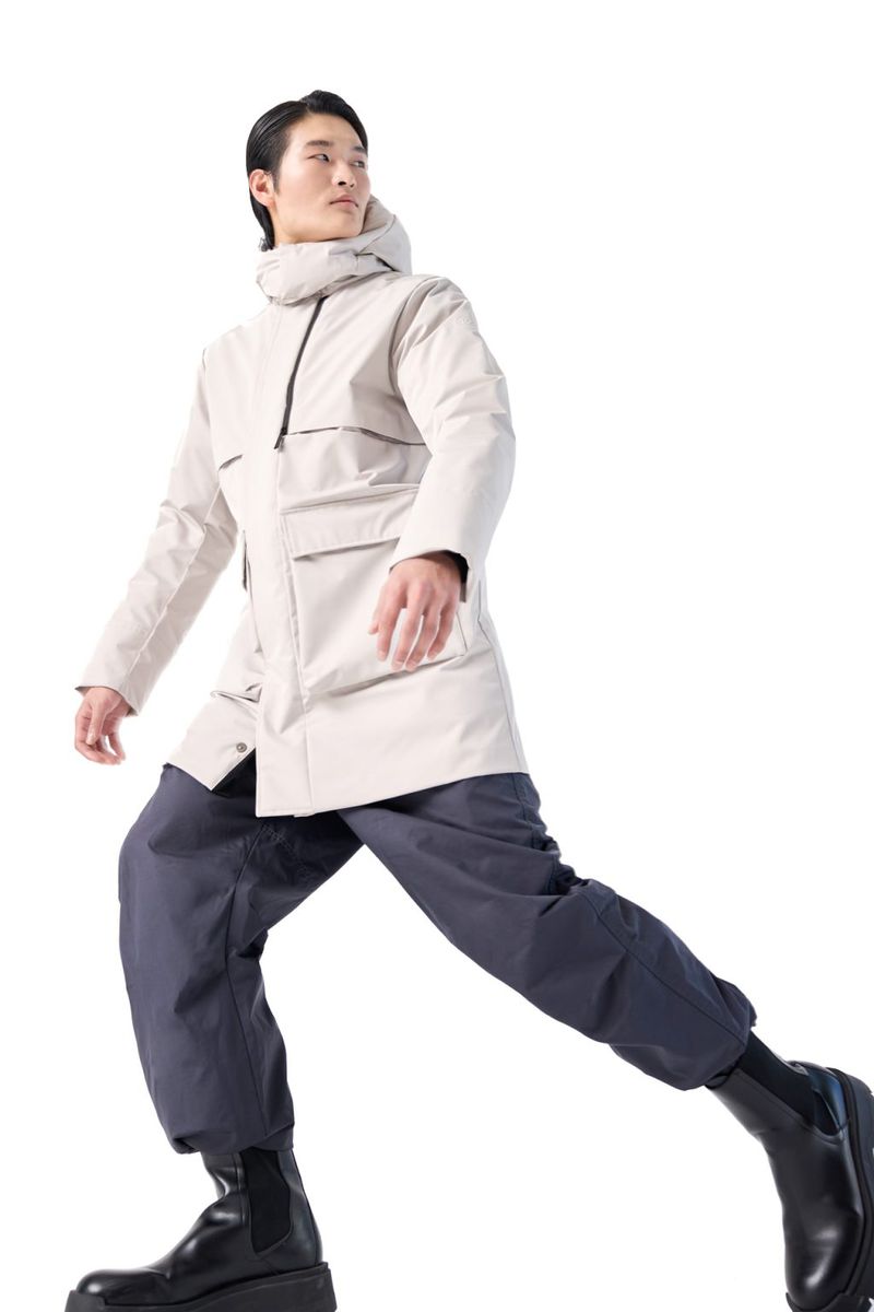 Asian male model in a beige hooded coat and dark pants walks on a white background, full figure studio shot, fashion style and studio shot.