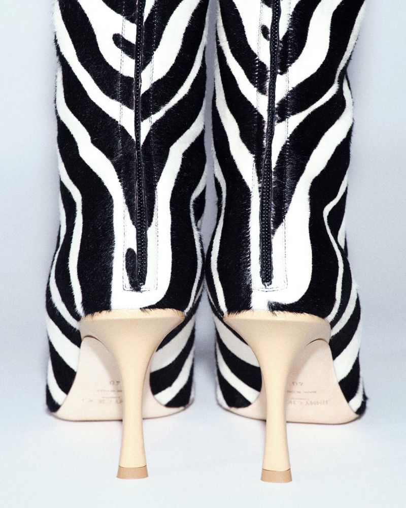 Close-up studio shot of knee-high, zebra-striped boots with stiletto heels against a bright white background, back view.