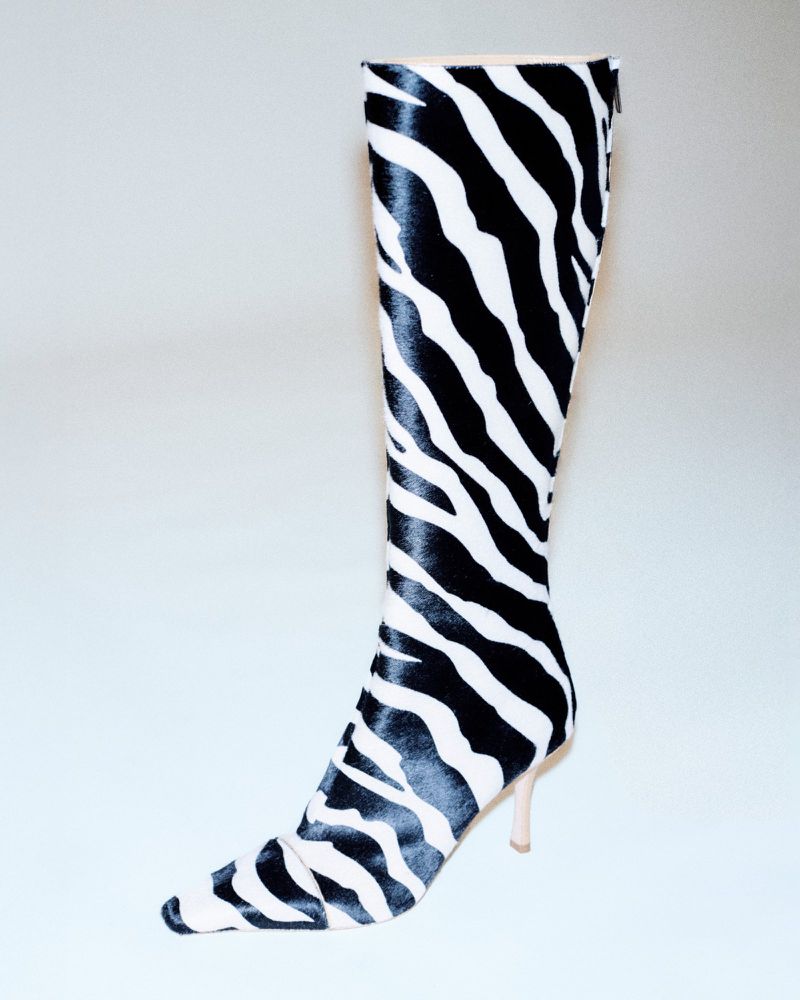 High-fashion knee-high boot with a stiletto heel, featuring a bold black and white zebra print pattern, presented on an isolated white backdrop.