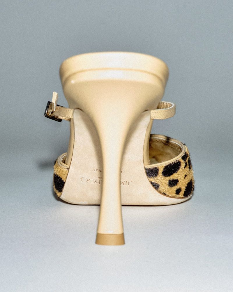 Close-up studio shot of a tan Jimmy Choo heeled sandal with a stiletto heel and a leopard-print design, angled from the back.