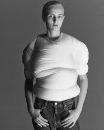 Model wearing an exaggerated white padded sculptural top and denim jeans against a grey studio backdrop.