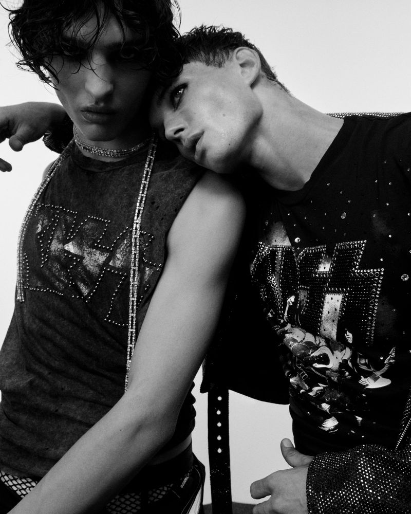 Two young adult men pose together in a close-up black and white studio shot, wearing band t-shirts and jewellery, showcasing fashion and style.
