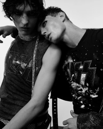 Two young adult men pose together in a close-up black and white studio shot, wearing band t-shirts and jewellery, showcasing fashion and style.
