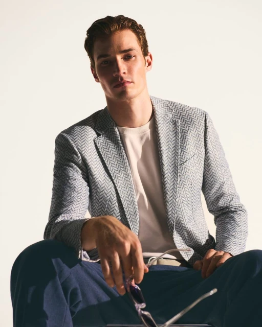 Portrait of a handsome man in a stylish blazer and slacks, sitting against a clean, bright backdrop in a fashion advertisement.