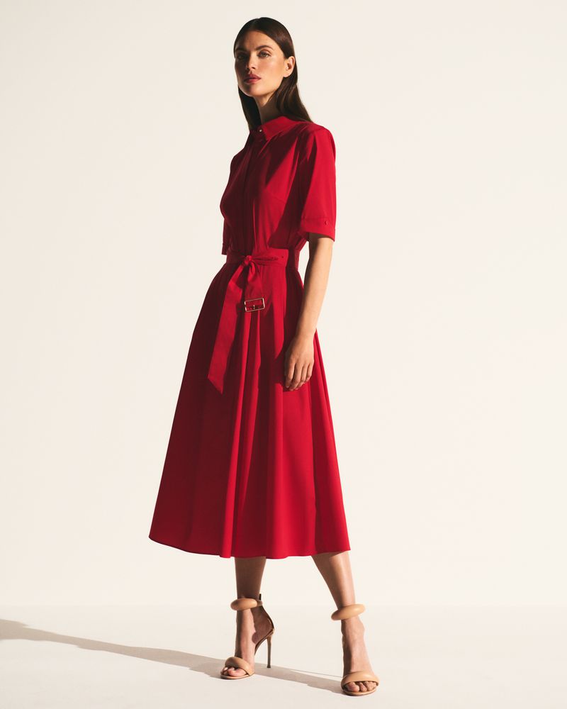 Woman in red midi dress with a-line skirt, belt, and short sleeves, standing in a photo studio with neutral-color stiletto heels.