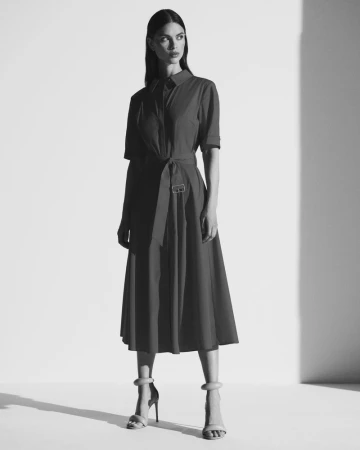Model wearing a belted short-sleeve midi shirt dress and ankle-strap high heels in black and white studio lighting.