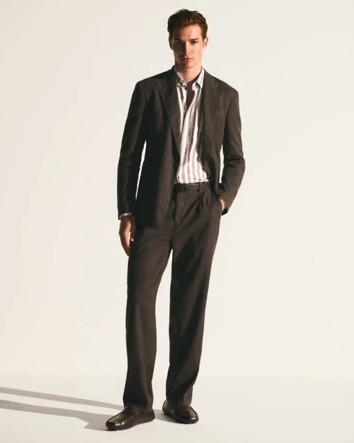 Full-length shot of a brown-haired man in a brown suit and striped shirt against a white background, fashion advertisement.