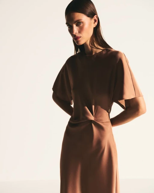 Indoor portrait of a single adult female fashion model in a brown dress, posing against a bright white background in a studio.
