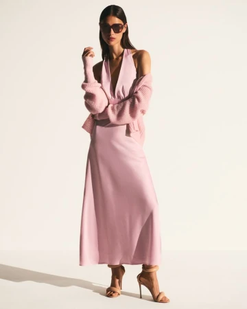 Model in a pastel pink halter dress, matching cardigan, oversized sunglasses, and nude stiletto sandals against a white background.