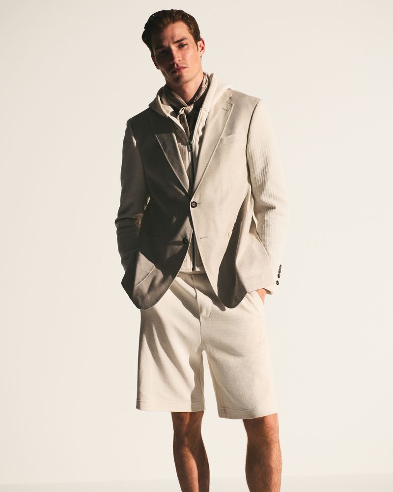 Fashionable man in beige suit jacket and shorts posing in studio. Light background, medium shot, style and confidence. 