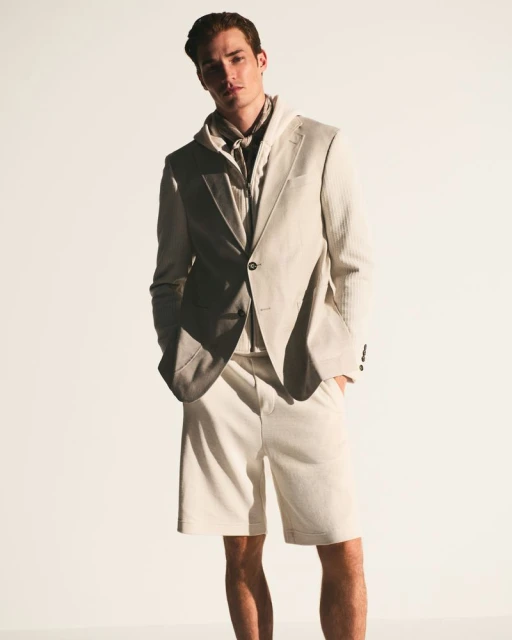 Fashionable man in beige suit jacket and shorts posing in studio. Light background, medium shot, style and confidence. 