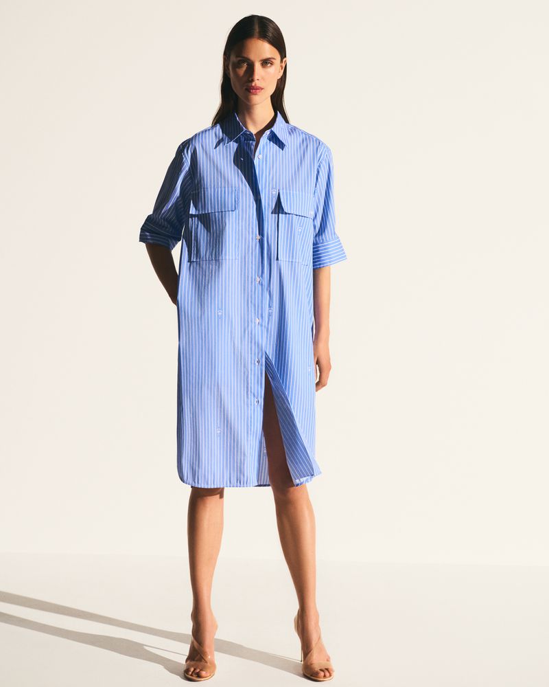 Full-length shot of a woman in a striped blue shirt dress and heels against a white backdrop. Fashion editorial content.