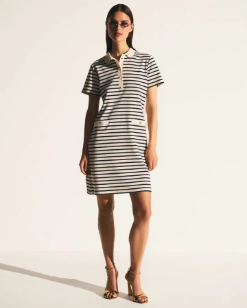 Model wearing a navy and white striped polo dress with gold high heel sandals against a clean white backdrop.