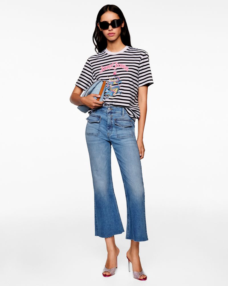 Model wearing a striped t-shirt, cropped flared blue jeans, dark sunglasses, and metallic heeled mules against a white background.