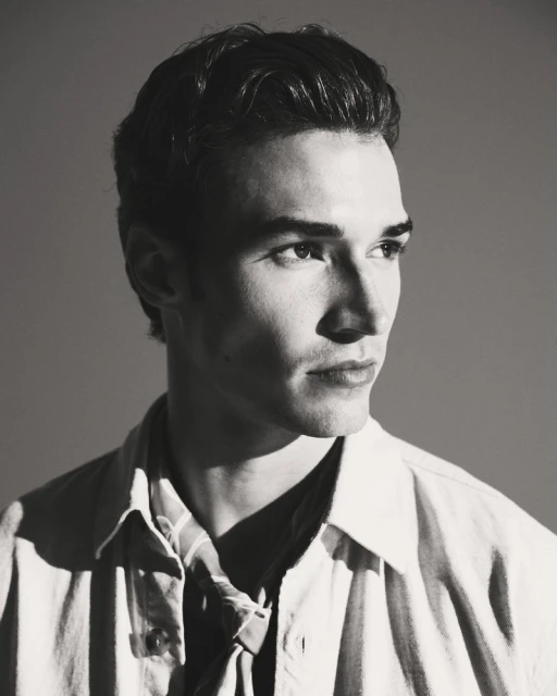 Monochrome portrait of a handsome adult male with short, wavy dark hair, wearing a striped shirt and jacket, looking away from the camera.