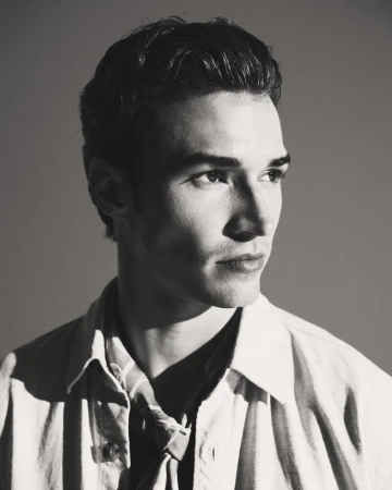 Monochrome portrait of a handsome adult male with short, wavy dark hair, wearing a striped shirt and jacket, looking away from the camera.