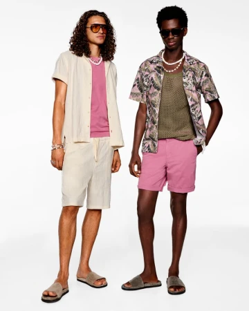 Two adult men wearing summer clothing and sunglasses in a bright studio setting, showcasing men's fashion.
