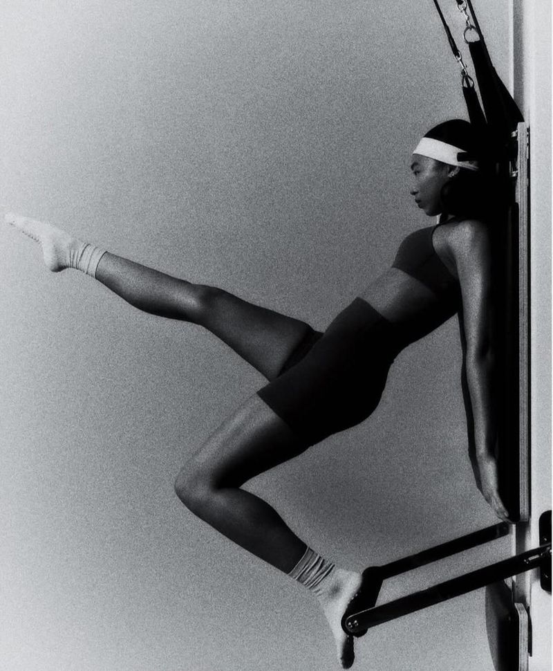 Woman in sportswear using exercise equipment for stretching in a black and white photo indoors against a light gray wall.
