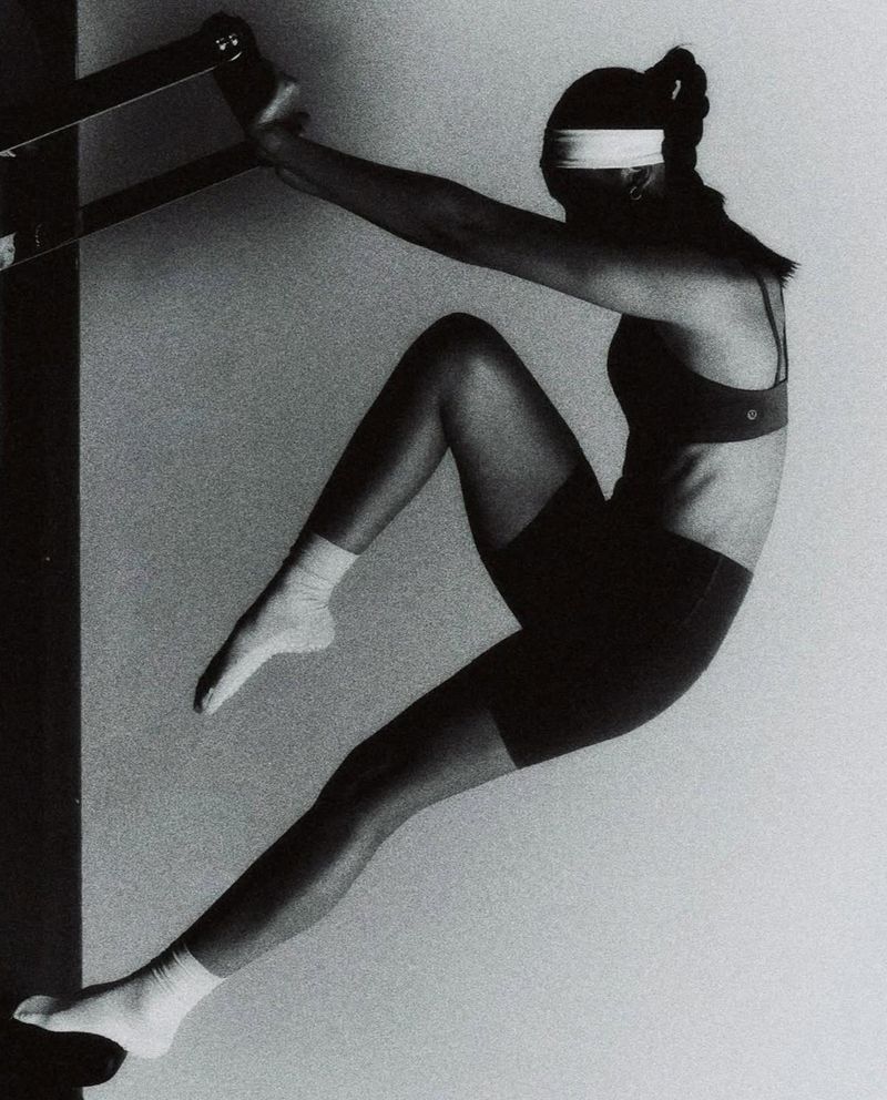 Athletic woman in sports bra and shorts doing inverted Pilates exercise using a wall-mounted ladder barre for core strength and flexibility.